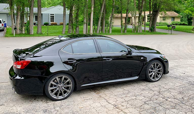 A black car is parked in a driveway in front of a house.