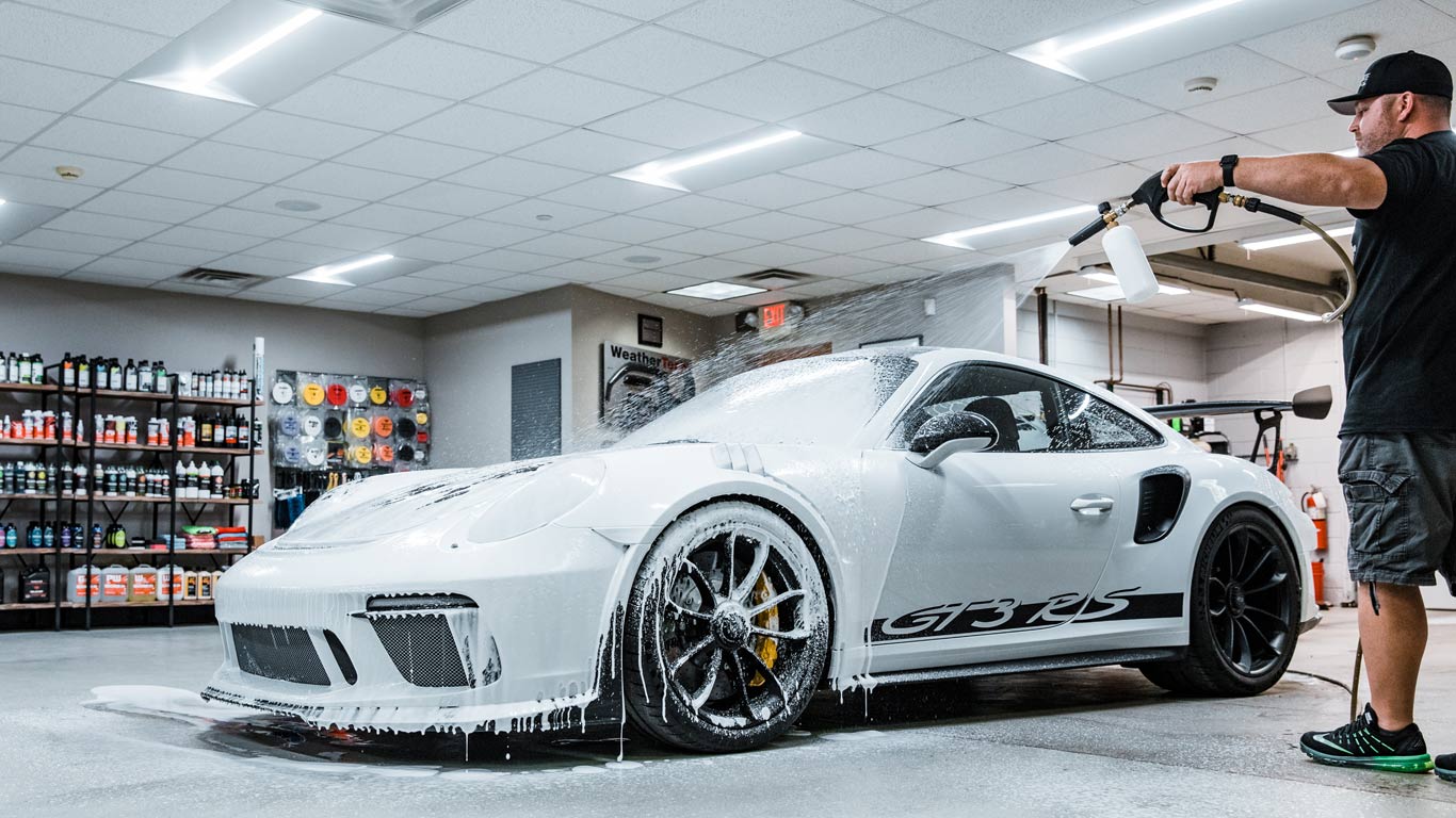 A man is washing a white sports car with a high pressure washer.