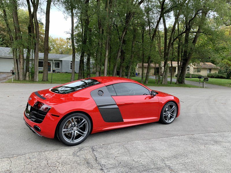 A red sports car is parked in a driveway with trees in the background