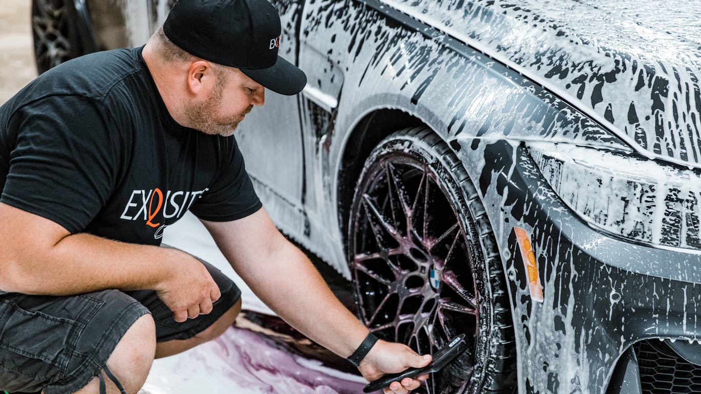 A man is kneeling down next to a car covered in foam.