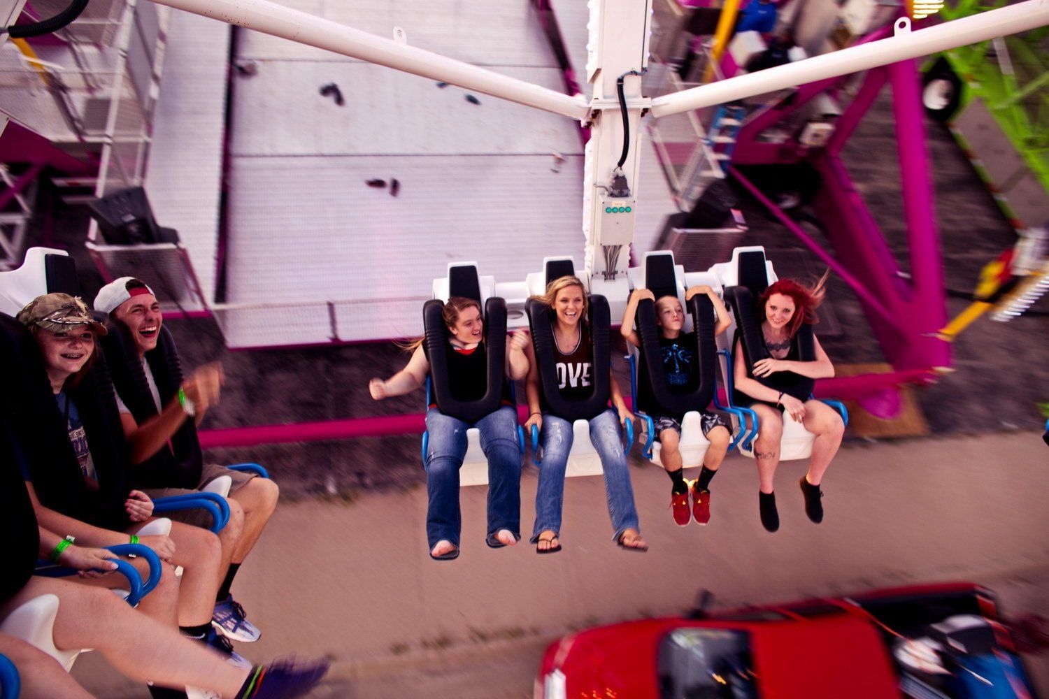Friends riding an amusement park swing ride high above the ground, laughing and hanging their feet over the scene below.