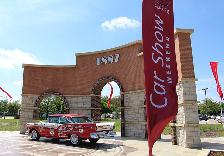 A red and white vintage car parked in front of a brick archway marked 