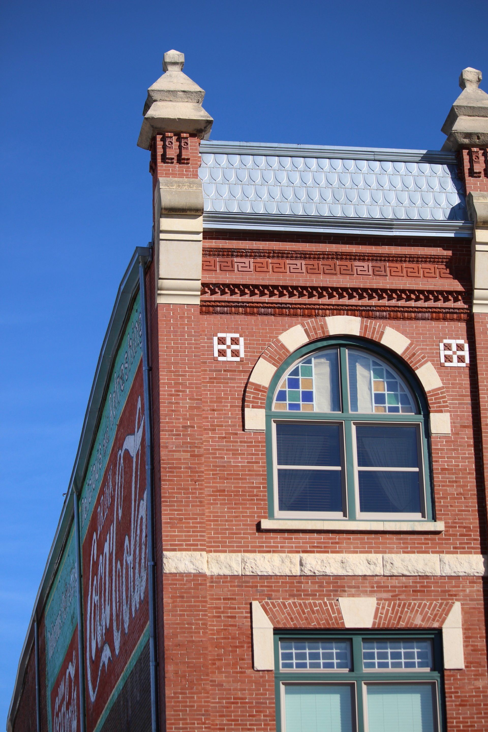 The brick upper facade of an old building featuring arched windows, stone decorative caps, and a vintage painted mural.