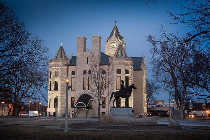 A stone courthouse with a clock tower stands at dusk, featuring a mounted equestrian statue in the foreground.