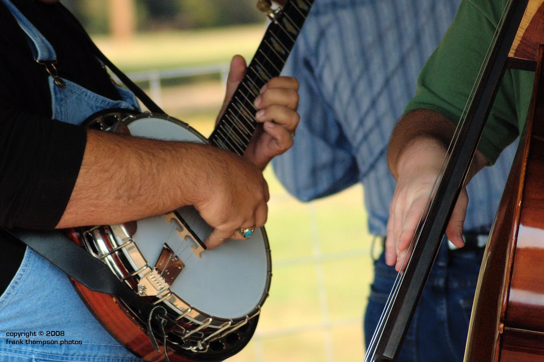 A musician playing a banjo with a second person standing nearby, possibly holding a stringed instrument.