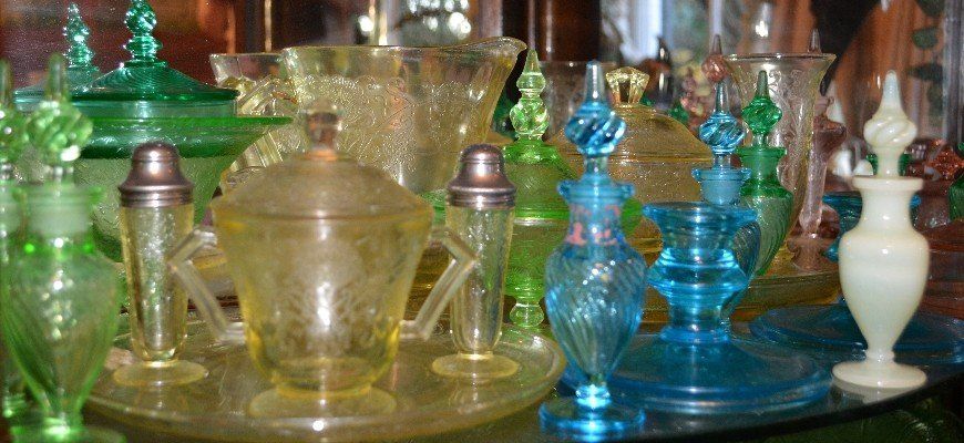 A collection of colorful vintage glass perfume bottles, bowls, and salt shakers arranged on a shelf.