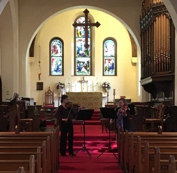 Two violinists performing in a church with stained glass windows and an organ.