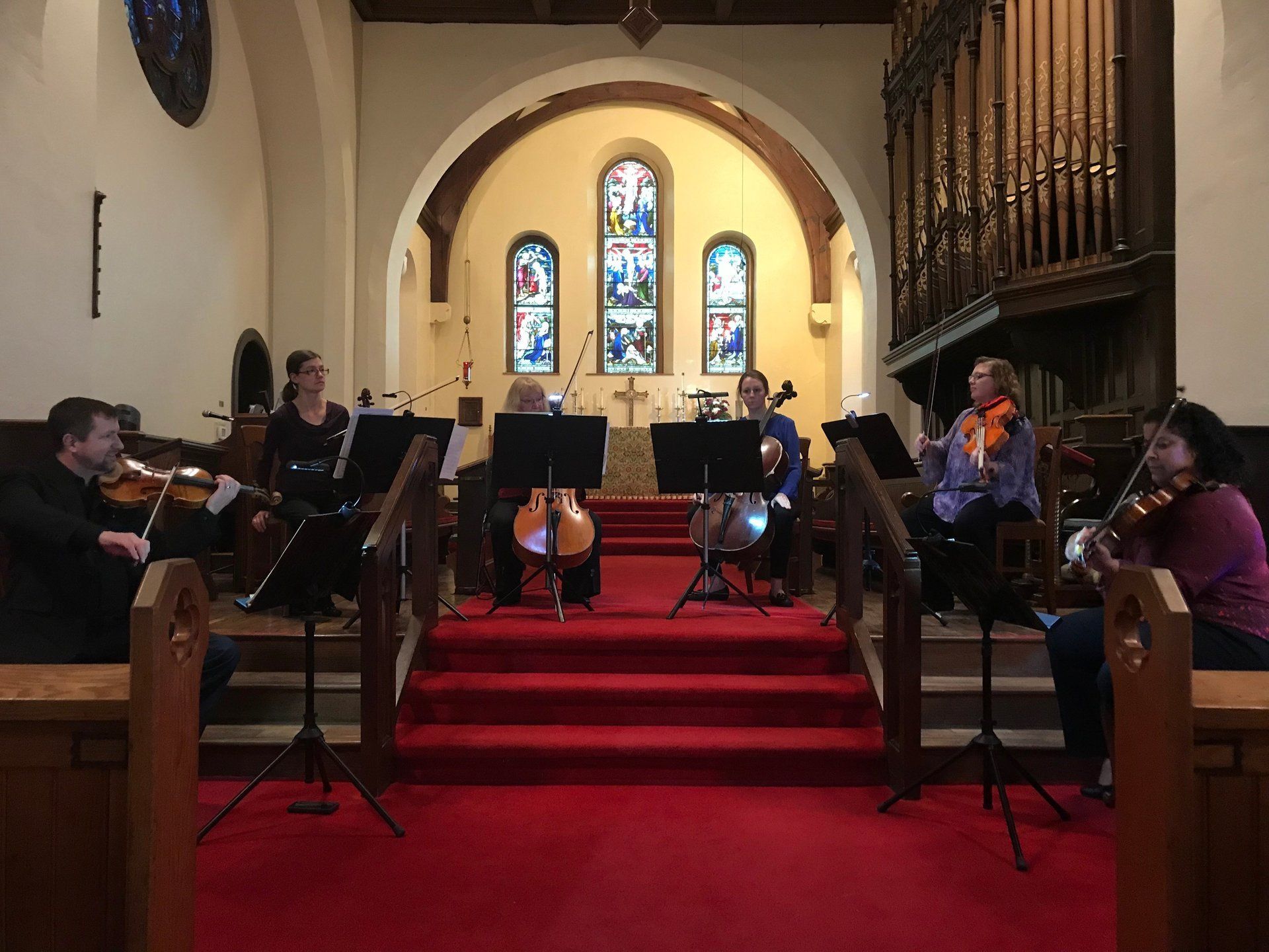 String quartet performing in a church with red carpet, stained glass, and organ pipes.