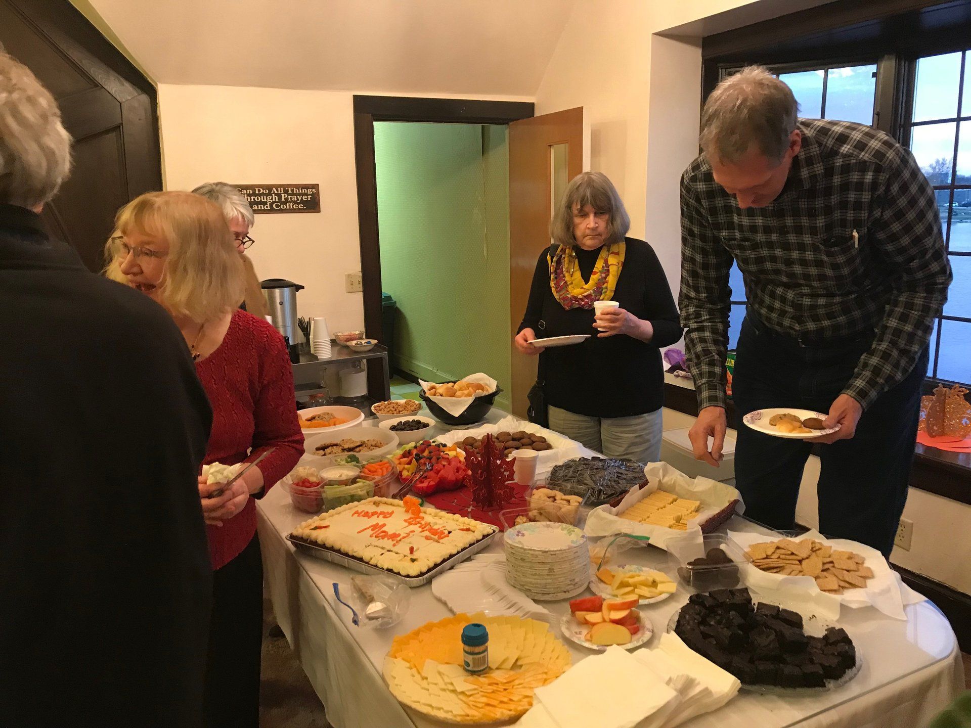 People at a buffet table, selecting food. Indoors, well-lit, with various dishes, cakes, and snacks.
