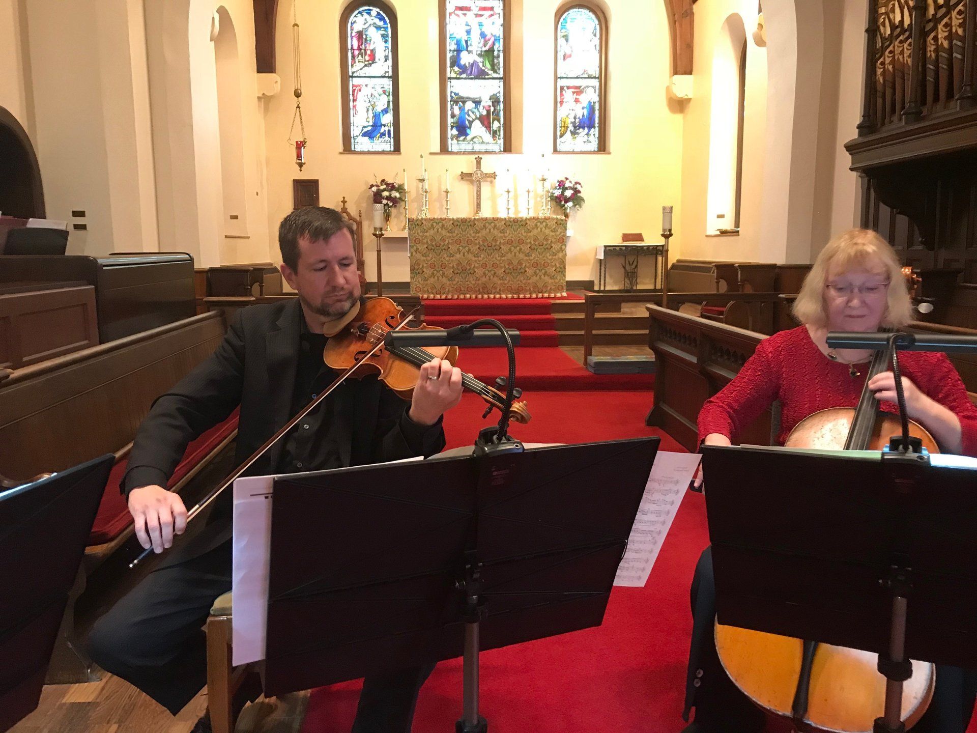 Two musicians playing instruments in a church: violin and lute. Red carpet, stained glass windows.