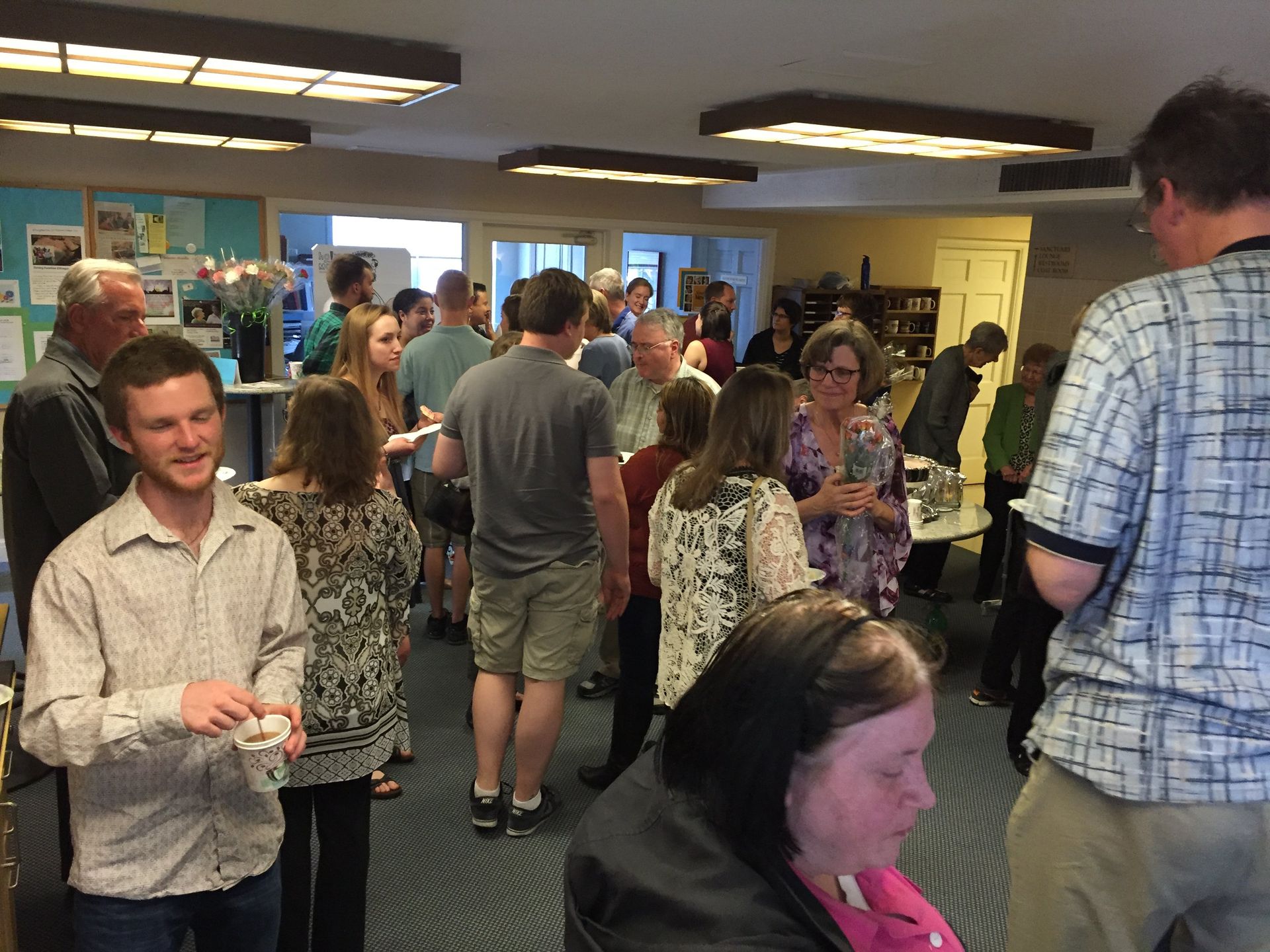 People at an indoor gathering, socializing. Many are standing, conversing, and holding items.