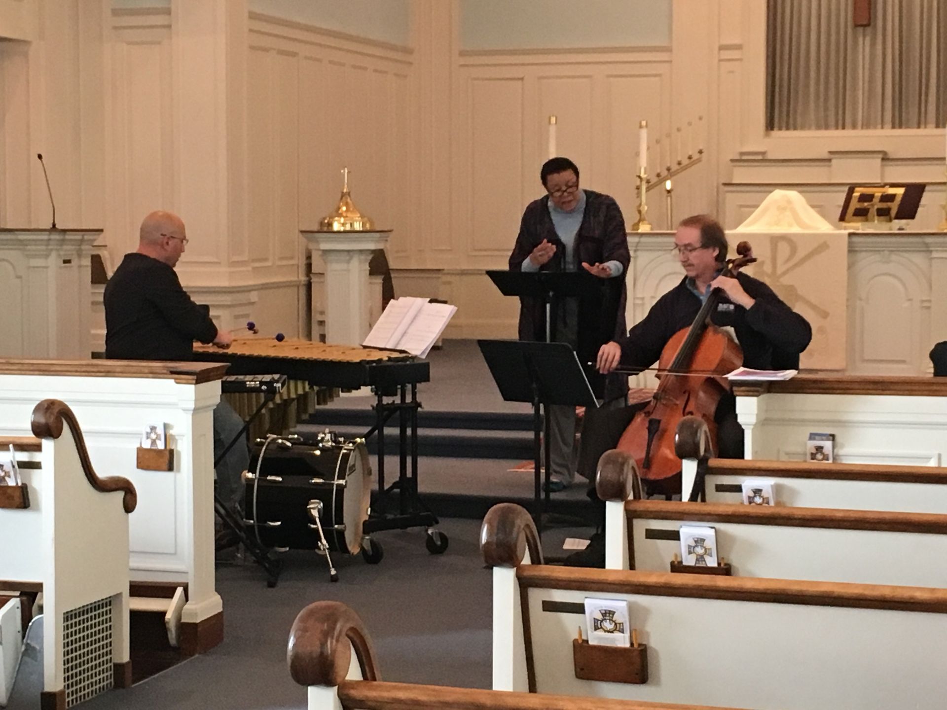 Three musicians performing in a church: a hammered dulcimer player, vocalist, and cellist.