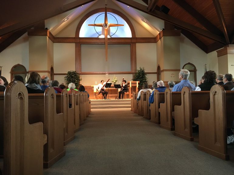 Church interior; two musicians on stage, cross above, audience in pews.