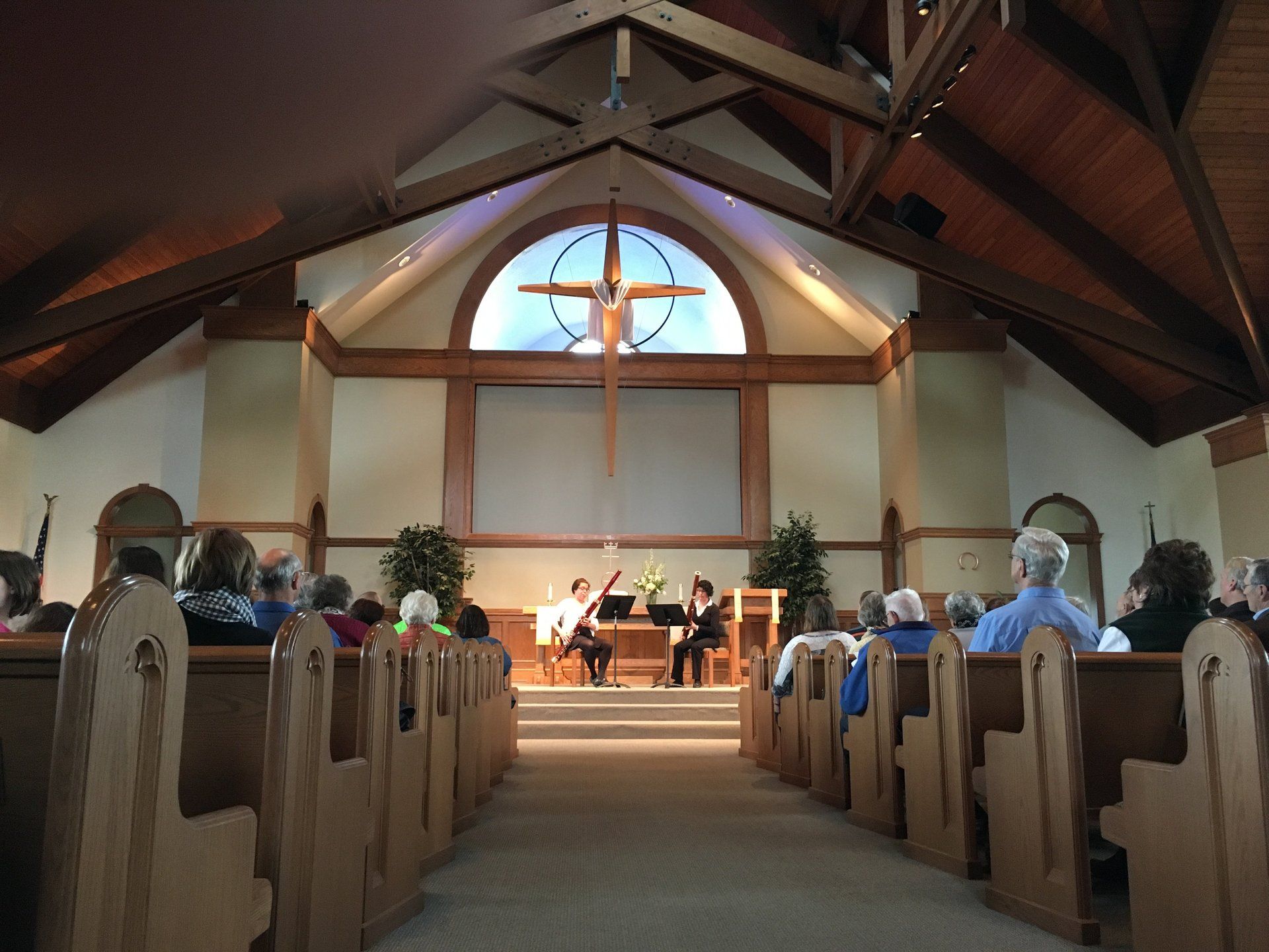Interior church view with musicians performing; people seated in pews. Cross above.