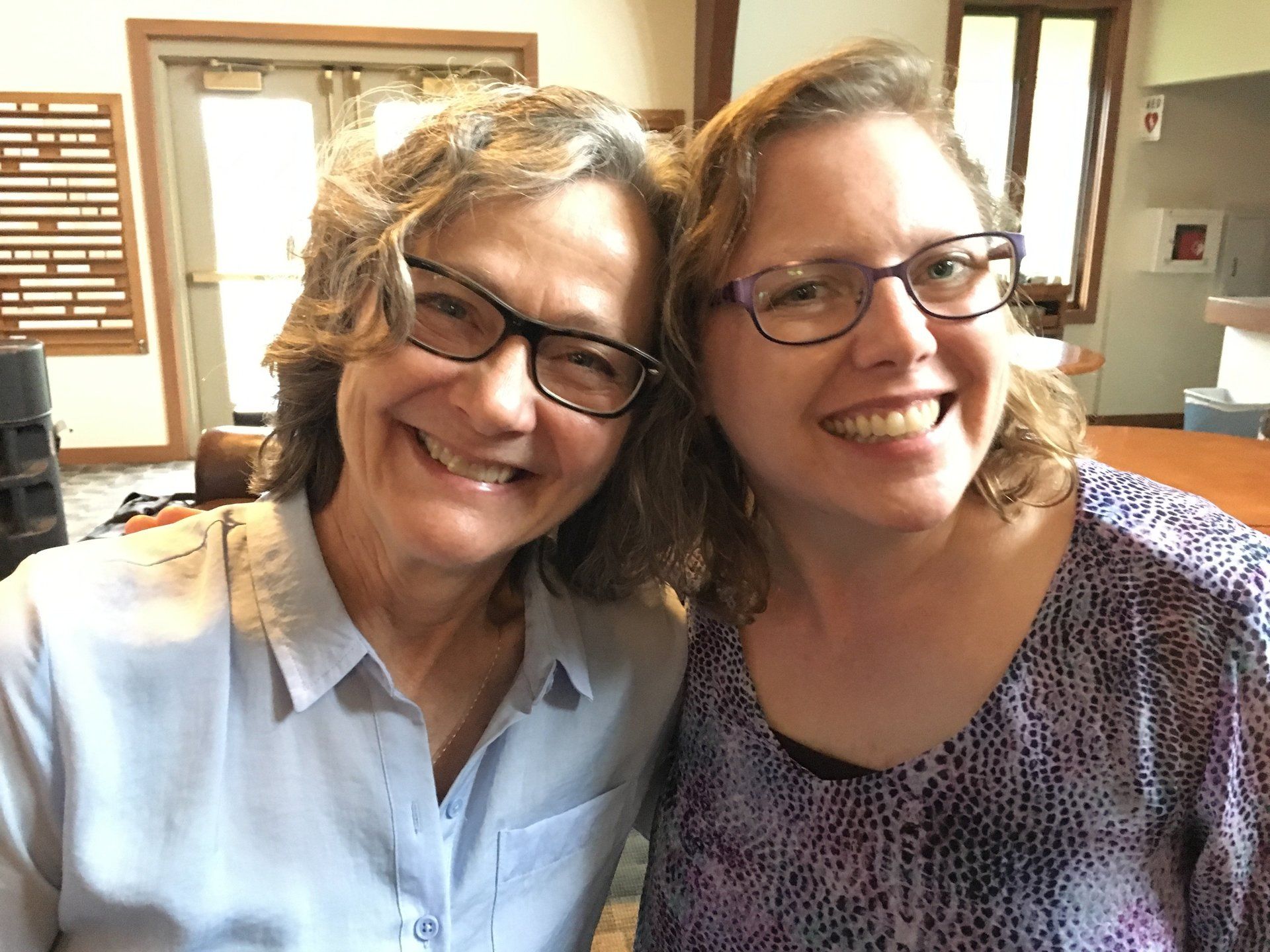 Two smiling people wearing glasses, indoors.