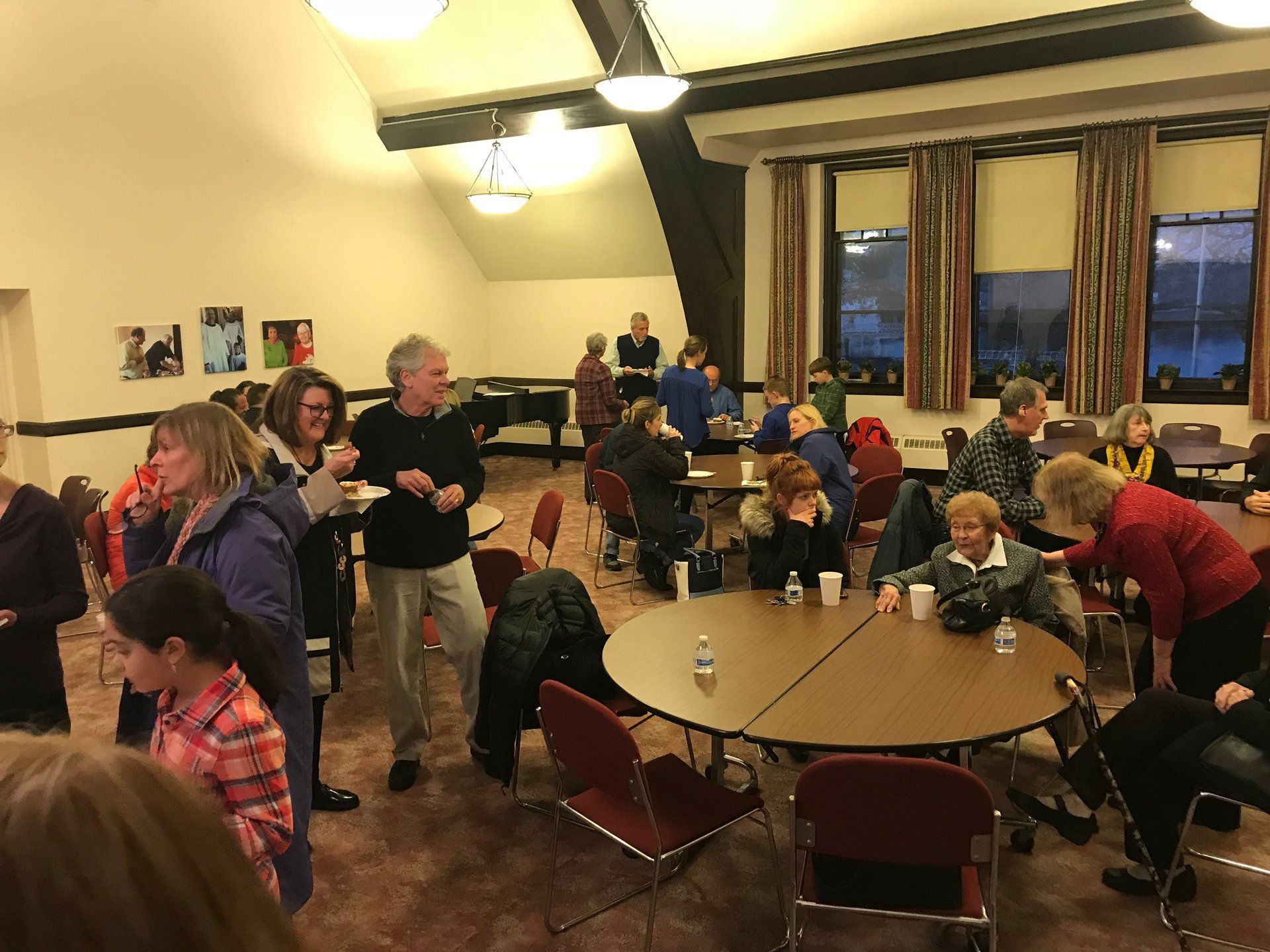 People gathered indoors at round tables, socializing and drinking beverages.