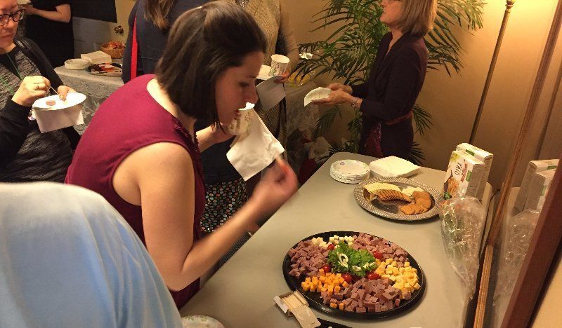 Woman in red dress eating from a table of snacks with others in a room.