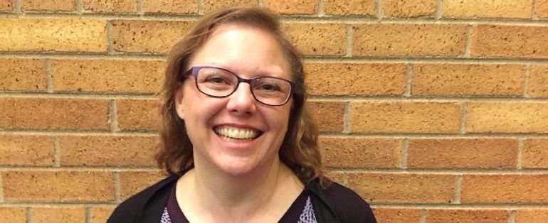 Woman with glasses smiling in front of a brick wall.
