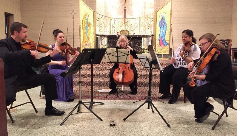 String ensemble performing in a church, five musicians with instruments in front of an altar.