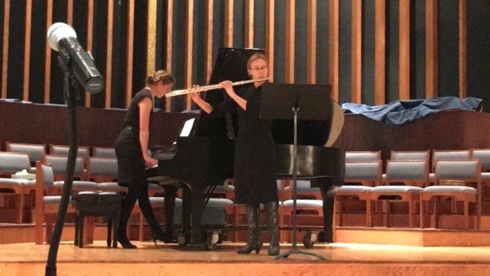 Woman plays flute with pianist, performance on stage.