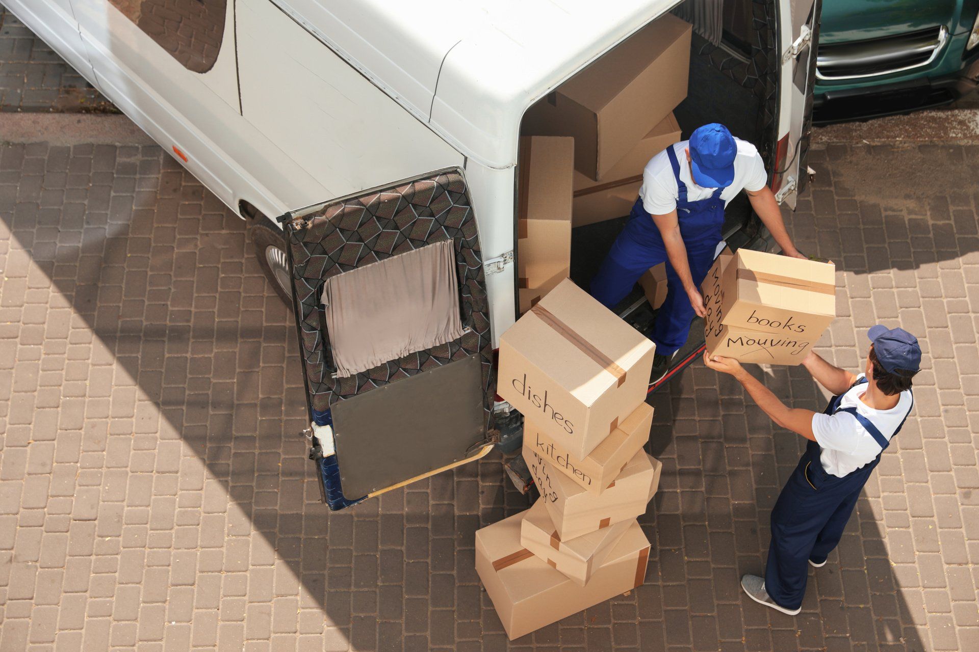 Two workers loading cardboard boxes into a white delivery truck from above