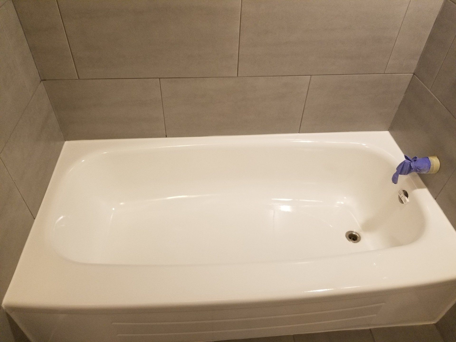 White bathtub against gray tiled wall. Chrome faucet with blue handle.