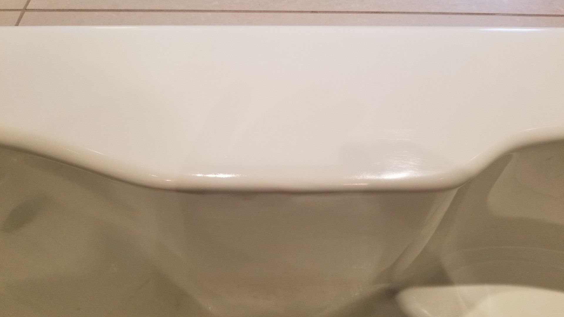 White porcelain bathtub rim with curved edge. Beige tile wall is visible in the background.