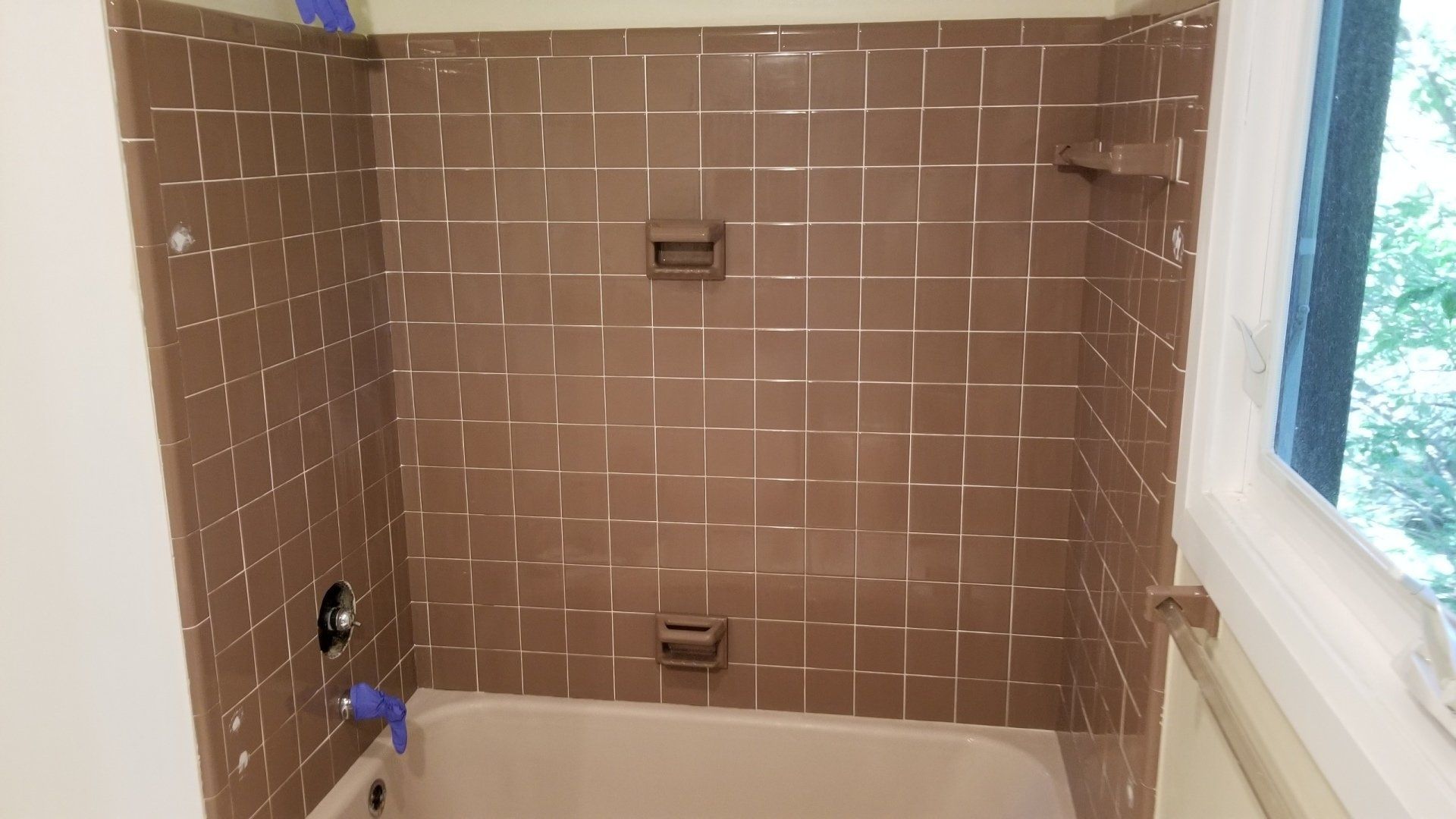 Brown-tiled shower with white grout, two soap dishes, a faucet, and a window to the right.