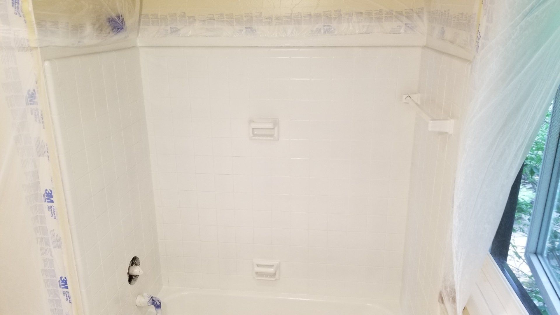 White bathtub with built-in soap dishes and shower rod. Protective plastic covers surrounding the bathroom.