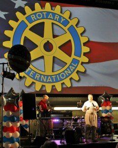 A man playing a guitar in front of a large screen that says rotary international