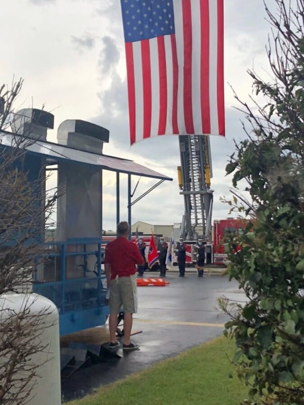 A man in a red shirt stands in front of an american flag