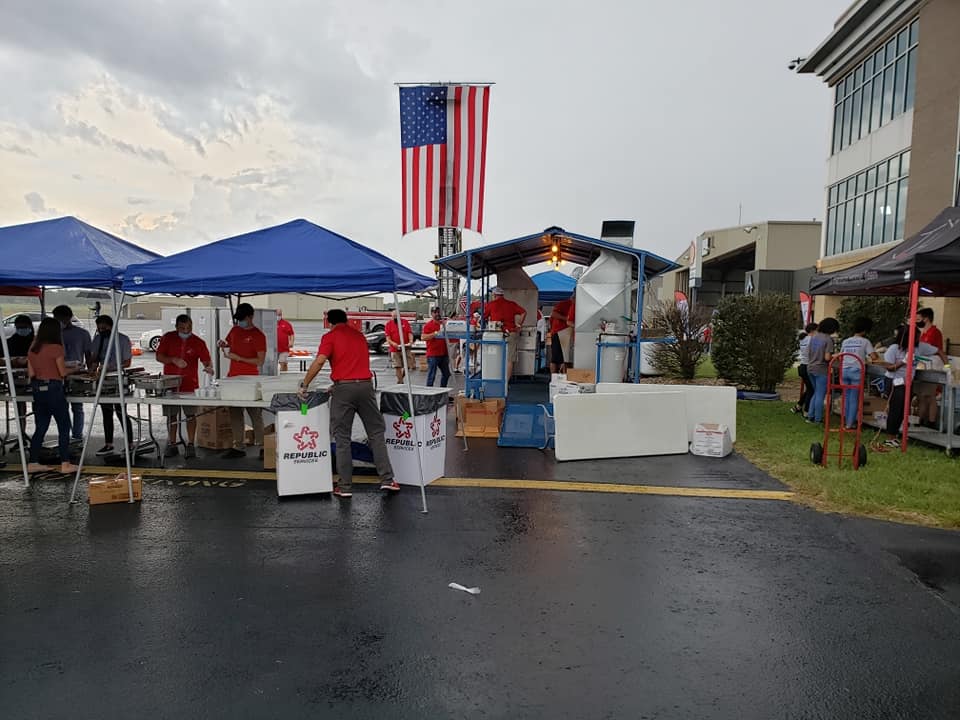 A group of people are standing around tables under tents in a parking lot.