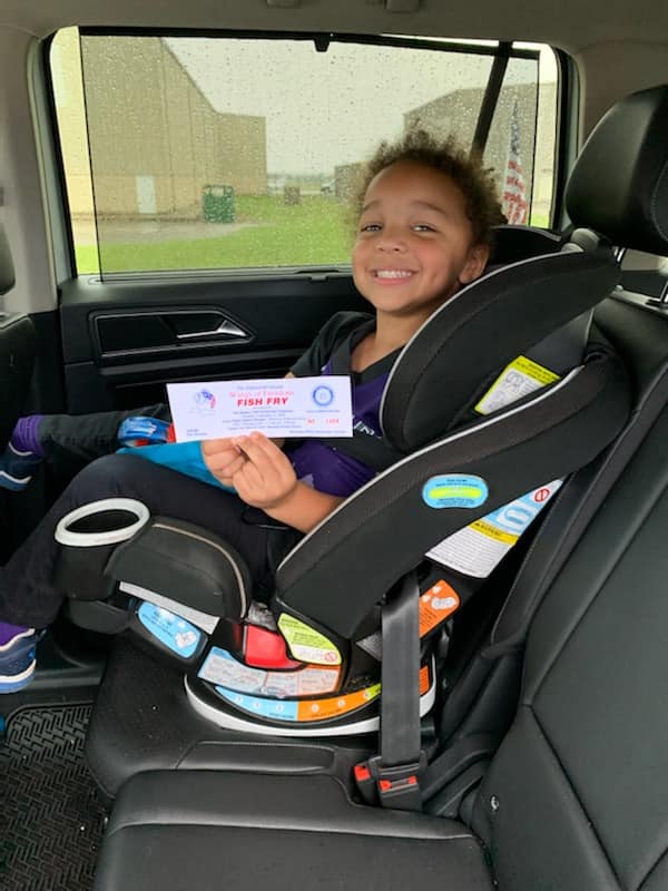 A little girl is sitting in a car seat holding a ticket.
