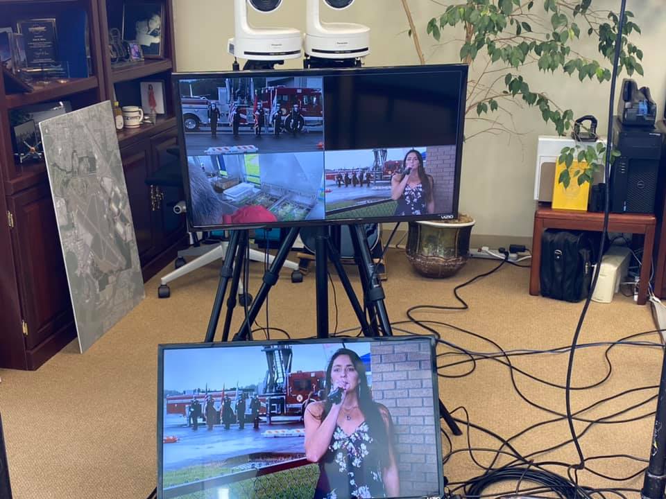 A woman is singing into a microphone in front of two televisions.