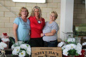 Three women are posing for a picture in front of a box that says shyrna 's