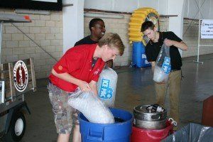 A man in a red shirt is pouring ice into a blue barrel