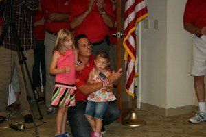 A man is kneeling down with two little girls in front of an american flag.