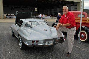 A man in a red shirt is kneeling next to a silver car.