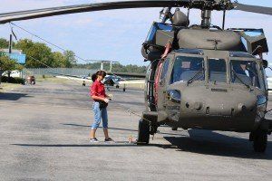 A woman in a red shirt is standing next to a military helicopter.