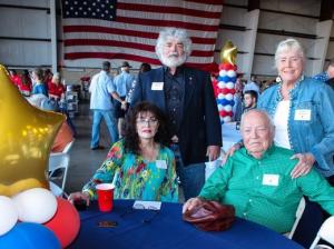 A group of people are sitting at a table with balloons in front of an american flag.