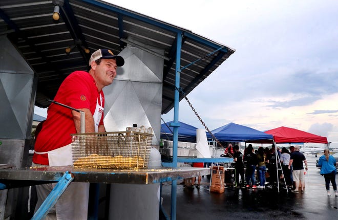 A man in a red shirt is standing in front of a fryer