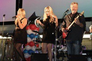 A man is playing a guitar while two women sing on stage.