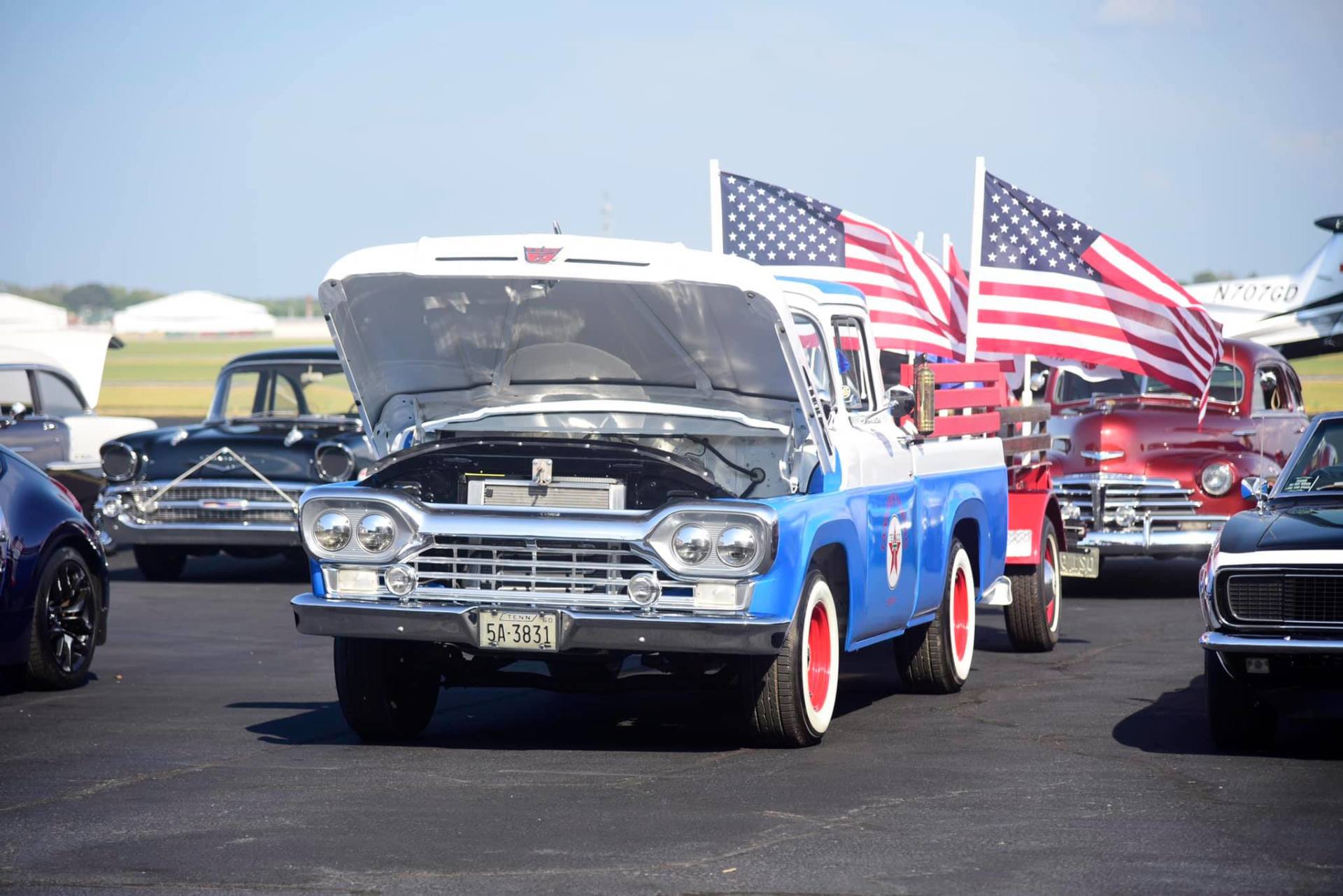 A blue and white van with the hood up is parked in a parking lot.
