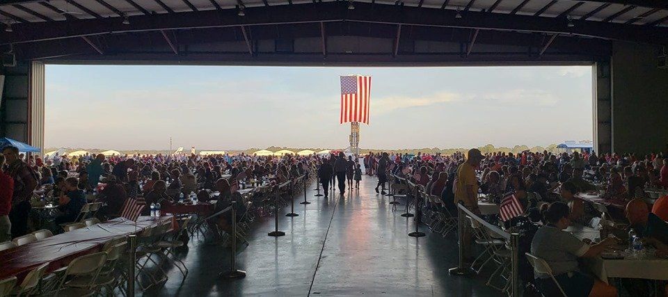 A large group of people are sitting at tables in an airplane hangar.