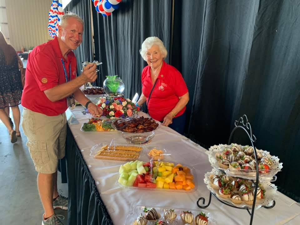 A man and a woman are standing at a long table filled with food.