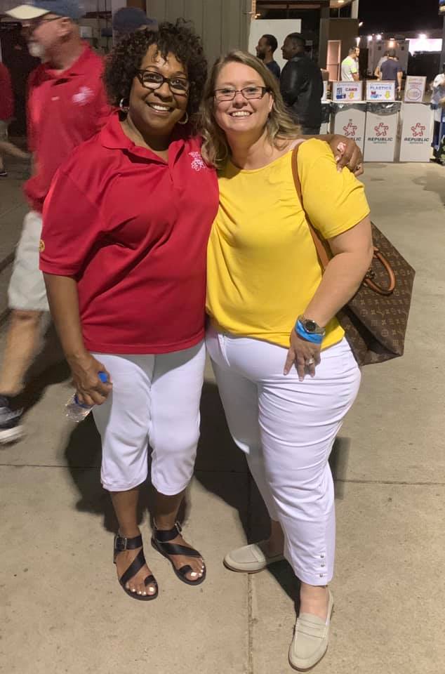 Two women are posing for a picture together on a sidewalk.