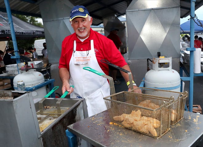 A man in a red shirt and white apron is preparing food in a fryer