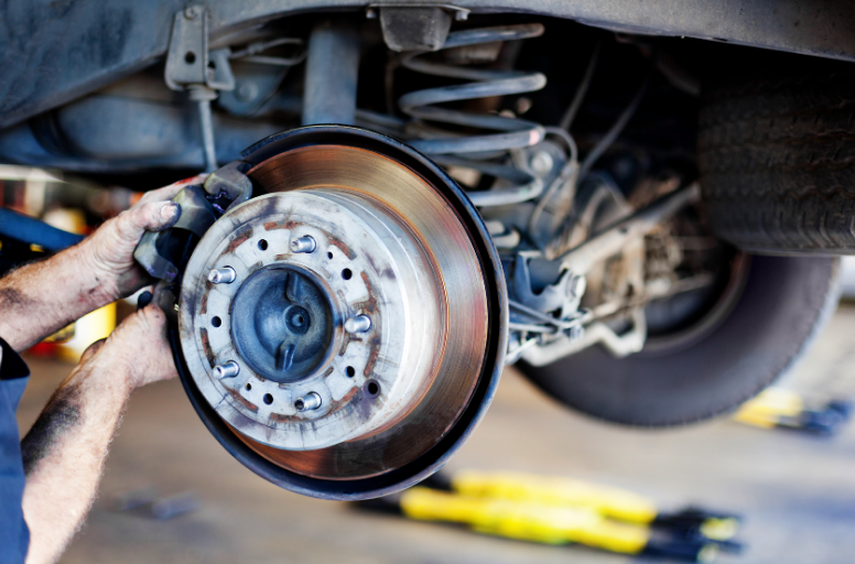 Mechanic removing a car’s brake rotor with a wrench under the raised vehicle.