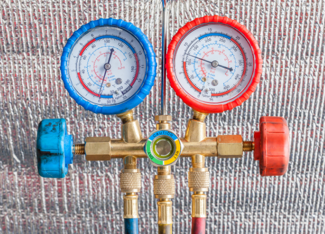 Blue and red HVAC manifold gauge set with hoses and brass valves on a textured surface