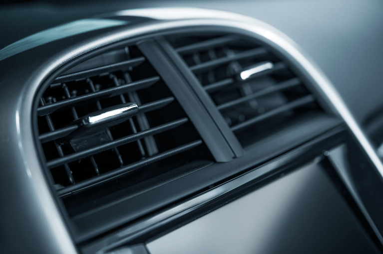 Close-up of a car dashboard air vent with black slats and silver trim